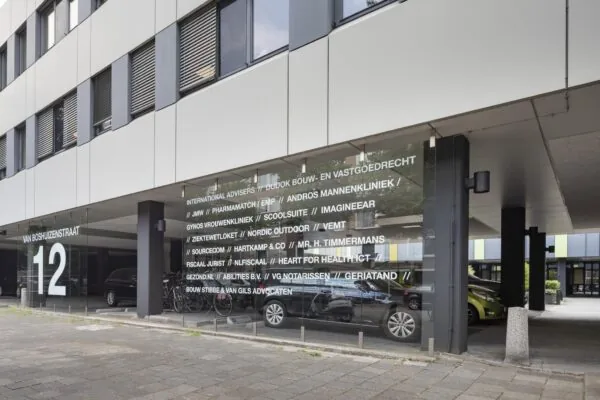 Ingang van een kantoorgebouw aan de Van Boshuizenstraat 12 met bedrijfsnamen op glazen gevel.